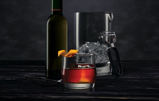 Cocktail mixing tools surrounding a Midnight Manhattan on a dark surface