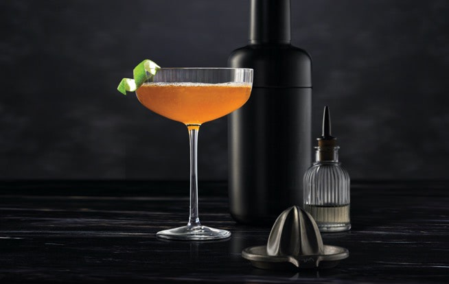 Cocktail mixing tools surrounding a Midnight Manhattan on a dark surface