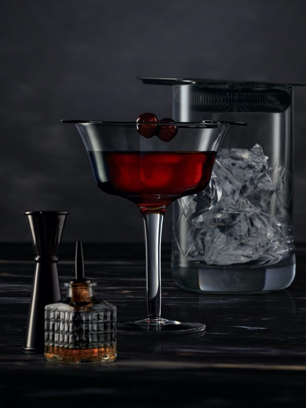 Cocktail mixing tools surrounding a Midnight Manhattan on a dark surface