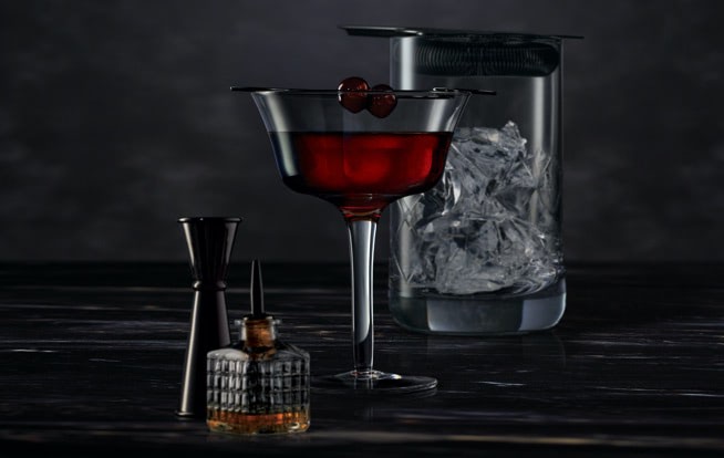 Cocktail mixing tools surrounding a Midnight Manhattan on a dark surface